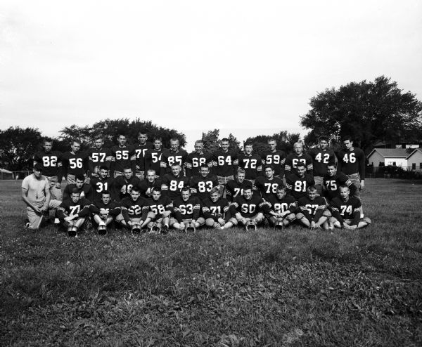 Outdoor group portrait of the 1954 Madison East High School football team, with Coach Herbert Mueller.