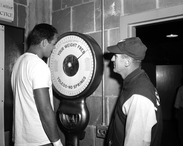 University of Wisconsin football captain Gary Messner steps on the scale as coach Ivan Williamson looks on.