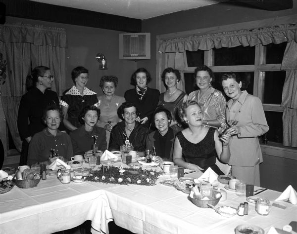Group portrait of twelve women, five seated at a banquet table and seven standing, attending the Madison Women's Municipal Golf Association banquet at the Cuba Club where golf skill prizes were awarded.