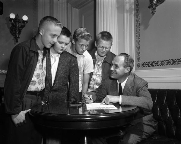 Governor Walter J. Kohler Jr. signs a document while four boys, probably newspaper carriers, look on.