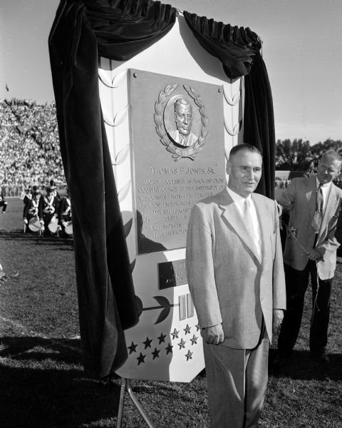 Thomas E. Jones, Sr. stands before the plaque that will honor him in the Wisconsin Athletic Hall of Fame in the Milwaukee Arena (now the U.S. Cellular Arena) during half-time ceremonies at the Wisconsin vs. Marquette football game at Camp Randall Stadium. He was the University of Wisconsin track and cross-country coach from 1913 through 1948.