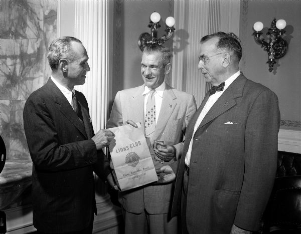 Governor Walter Kohler buys the first bag of light bulbs from Ed Steul (center), Madison, Lions' district governor; and H. M. Schmid (right), New Glarus, chairman of the Lions' Leader Dog state committee. Profits from the light bulb sale go to the Leader Dog for the Blind organization and other Lions projects.
