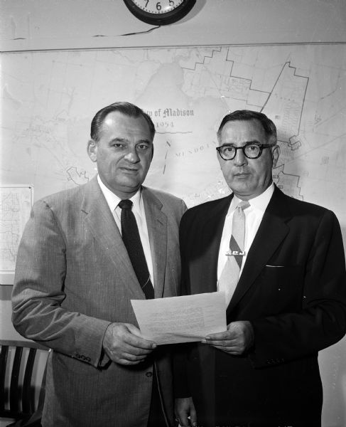 Two men stand in front of a map of Madison with a document for Oil Week.