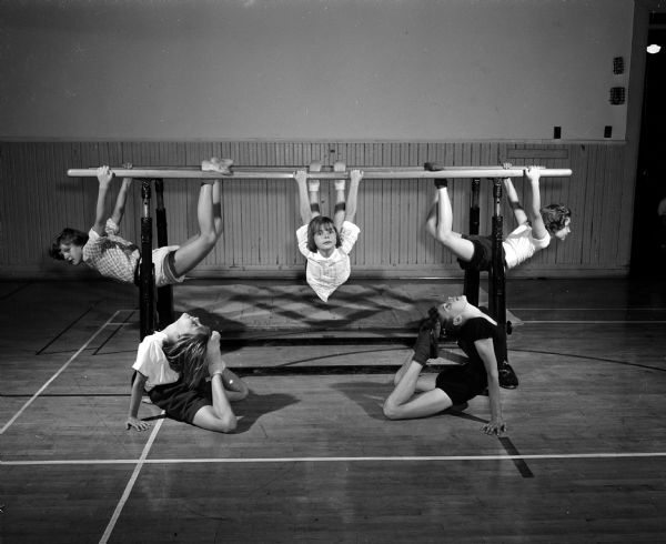 Children practice a parallel bar routine for the Madison Turners program for their 1955 Centennial Celebration. Left to right on bars: Judy Hoppmann, Elizabeth Wittrock, Connie Ruff.  On floor: Kathy Wittrock and Gloria Goldbin.