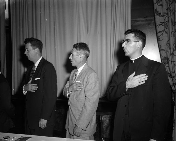 Three men, including a clergyman, say the pledge of allegiance during a retail clerks meeting.