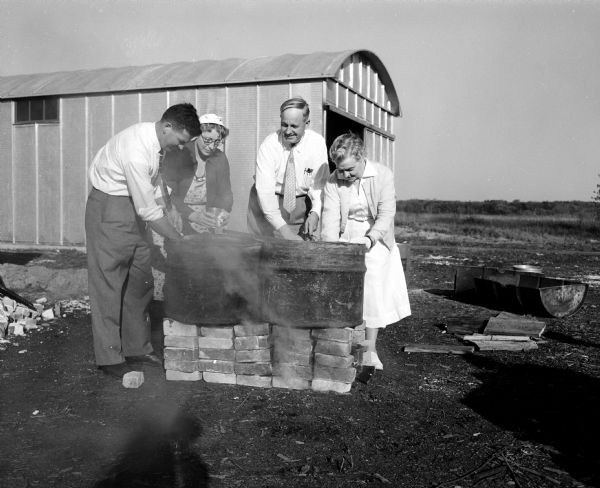 Robert Nuckles (left); Mrs. Earl Siggelkow, McFarland; George Solsrud; and Laura Palmer washing dishes in halved oil drums during a Civil Defense emergency mass-feeding practice.