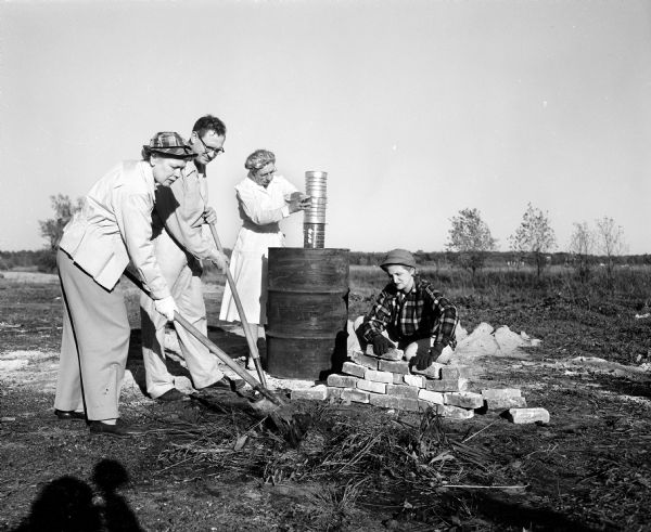 Mrs. Ryerson (left) and Melvin Dykman use shovels to build a brick stove during a Civil Defense emergency mass-feeding practice. Katheryn Henning stacks large cans for a chimney, and Erma Smith stacks bricks.
