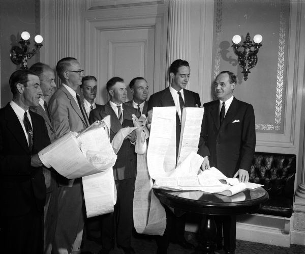 Governor Walter Kohler being is presented with a 147-foot petition bearing signatures of 5,000 area residents seeking to ban the diversion of sewage from the Madison Metropolitan Sewerage District into Badfish Creek. Left to right: Chester Murwin (Fulton), R.W. Bliss (Janesville), Stanley Witzel (Union), David Blanchard (Edgerton), Lloyd Stearnes (Porter), Louis Falligant (Edgerton), and Gov. Kohler.