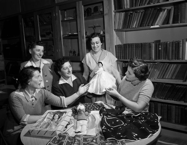 Five women admire some dolls as they prepare items for their annual public bazaar. Seated left to right, are: Judith Stein, Mrs. George Stewart, and Roslyn Kopelberg. Standing are: Mrs. Stanley Cohen and Belle Novick.