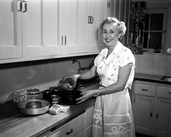 Mary Huber standing in her kitchen while fixing a molded jello salad in preparation for a University of Wisconsin football pregame party. She will be serving fried chicken as the main dish.