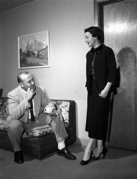 Stewardess Mary Ogle models a wool suit she made. Looking on is Bill Domres, formerly a steward for North Central who became a station agent when the airline replaced stewards with stewardesses. The photograph was taken to accompany an article about the daily lives of six North Central airline stewardesses assigned to Madison as their home base.