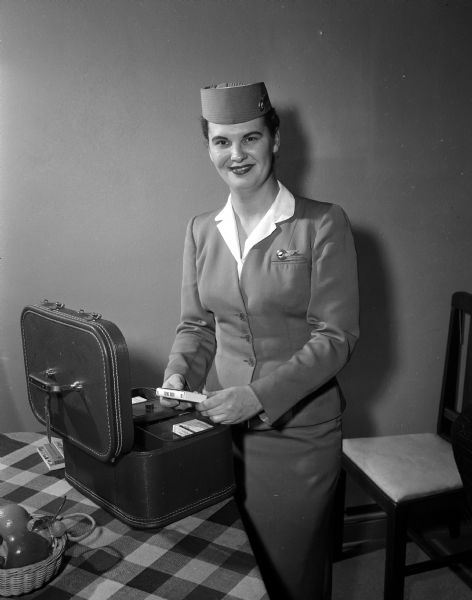 Dolores Wisnauskas, wearing her stewardess uniform, checks an overnight case fitted with first aid supplies. The photograph was taken to accompany an article about the daily lives of six North Central airline stewardesses assigned to Madison as their home base.