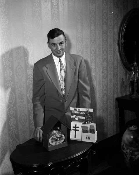 Stanley F. Tucker, chairman of the annual Christmas seal sale to fight tuberculosis, diplays samples of the wishing wells made by volunteer workers at Lake View sanatorium. These will be placed in various restaurants and bars for donations. The self-serve boxes will be placed in branch postal stations, hospitals, and drug stores.