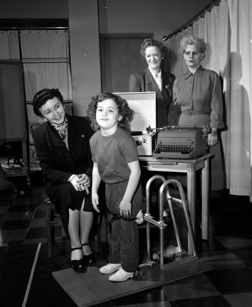 Representatives of the Pythian Order of the State of Wisconsin present equipment to the Washington Orthopedic School at 545 West Dayton Street. Mrs. Marie Evans, Alma (seated), the 1954-55 Grand Chief, demonstrates a new stabilizer to one of the school's pupils.
Standing is Mrs. Eva W. Kuhlman of 451 North Few Street (left) and Mrs. Daisy Schara, 1921 Fisher Street. Both are officers in the state organization. Aid to crippled children is the top project of the Pythian Order; other gifts were also given.