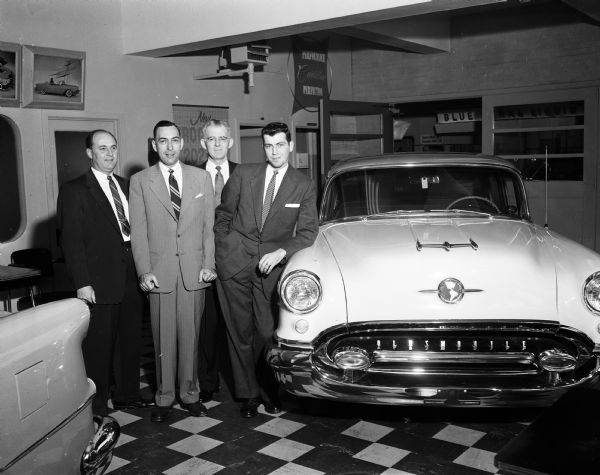 Four salesmen pose near an Oldsmobile car inside the showroom at the Pyramid Motor Company at 434 West Gilman Street.