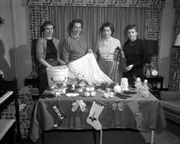 Four ladies of the Rosary-Altar Society at Blessed Sacrament Catholic Church display items for their annual Christmas bazaar. From left are: Mrs. Arthur (Harriet) Raffill, Mrs. Wilbur (Alice) McGuire, Mrs. R.D. (Ernestine) Wagner, and Mrs. A.H. (Gertrude) Spevacek.