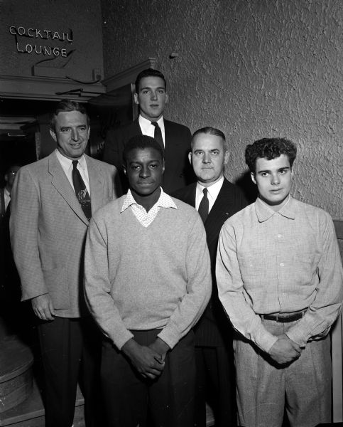 Group portrait of participants recognized at the annual banquet for the Madison Central High School football team. In the back is University of Wisconsin football player Bob Gingrass, the event's main speaker. Others pictured, left to right, include: coach Harold Pollock, co-captain Dick Harris, sponsor Bank of Madison vice-president Theodore Meloy, and co-captain and most valuable player Louis Cassini.