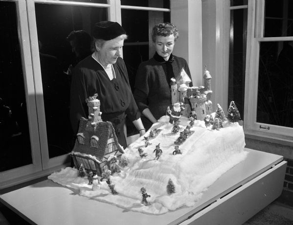 Mrs. Ewin B. (Rosa) Fred and Mrs. Robert C. (Isabel) Clark admire the Christmas decorations created by Mrs. George M. (Vivian) Werner for the Christmas tea of the Daughters of Demeter. Mrs. Fred is the wife of the University of Wisconsin president and hostess of the tea.