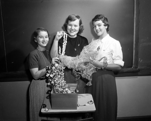 Three girls displaying Christmas decorations that their club had made for the Veterans' Administration Hospital. They are Judy Davis, Heidi Trummer, and Marion Freed.