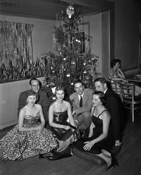 Three of the committee members for the annual Christmas dance given by the Interns and Residents Wive's Club of the University of Wisconsin Hospitals pose in front of a Christmas tree with their husbands at the Blackhawk Country Club. From left, the couples include: Dr. and Mrs. David McGrath, Dr. and Mrs. Douglas H. White, and Dr. and Mrs. James W. Manier.