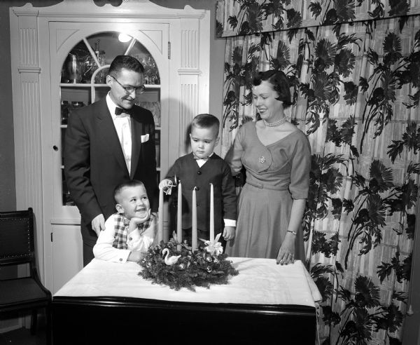 J. Kenneth and Mary Conlin and their sons light an advent wreath in preparation for Christmas. Left to right: J. Kenneth; Kevin age 3; Thomas (lighting the candle), age 5; and Mary.