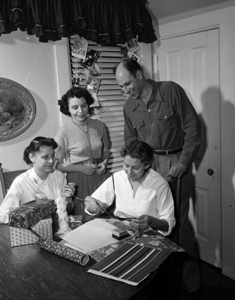 Josephine Chance (lower right), of Barnsley, Yorkshire, England, is shown wrapping presents for "Boxing Day," a December 26th observance day on which English householders give presents to those who have served them. Miss Chance was one of the four American Field Service scholarship students living in the Madison area. Shown looking on is her host family; they include Sue, Aileen, and Richard Lueth.