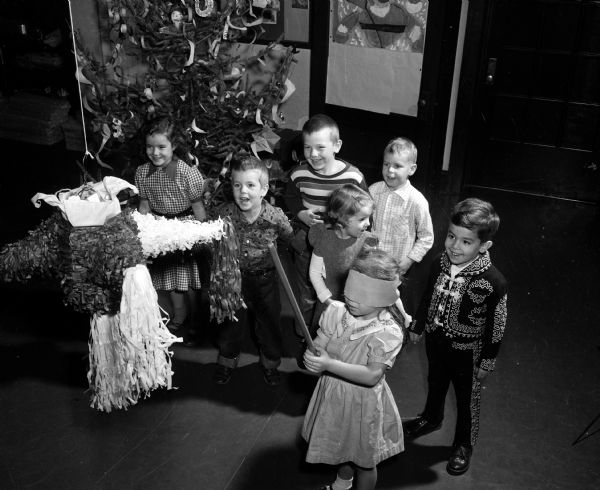 Edmundo Calva, son of Dr. and Mrs. Edmundo Calva of 1603 Jefferson Street and formerly of Mexico City, brought a pinata to Miss Marguerite Drews' morning kindergarten class at Randall School. Edmundo, wearing a Mexican suit, is at right, watching Cheryl Laska of 1323 Randall Court, trying to break the pinata. Other kindergarteners, left to right, are Kathleen Williams, 113 North Spooner Street; David Foster, 2842 Regent Street; Timothy Noll, 2127 Commonwealth Avenue; Trudy DeMuth, 10 Lathrop Street, and Tommy Ruland, 205 North Franklin Avenue.