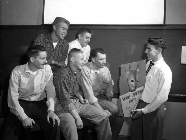 Six members of the 20-man "cutting crew" for West High School's annual Senior Dance receive instructions for the party. Dick Musselman, 402 Laurel Lane, shows a poster for the party to (front row) David Esser, 57 Merlhan Drive, Jerry Olson, 237 East Sunset Court, and Arlyn Jones, 4101 Hillcrest Drive. The two boys in the back are Fred Mohs, 3616 Lake Mendota Drive, and Al Miller, 1903 Lake Mendota Drive.
