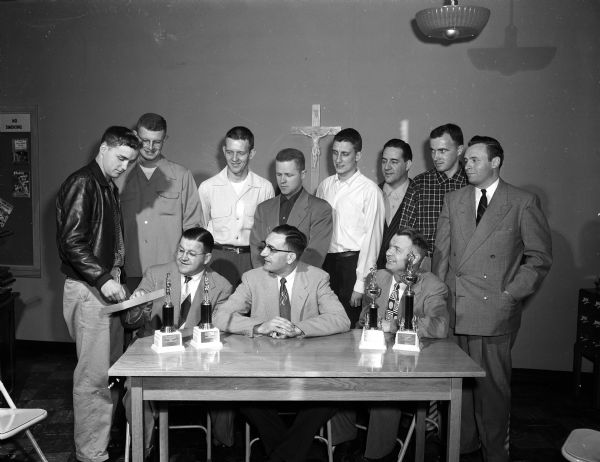 Drawings for the annual St. Bernard's amateur basketball tournament were made at a meeting. Managers of the eight competing teams met with tournament officials. Left to right are, seated: Vic Gruendler, Charles Lutz and Ray Busse. Standing are: Ralph Chamberlin, The Hub; Jack Wise, Randall State Bank; Tom Schmitz, Middleton; Don (Gus) Burwell, Tipler's Transfer; Dick Stem, The Pub; Max Gordon, Madison Accordion Center; Jim Busrchinger, Brathaus; and Jack Swanton, Gulesserians.