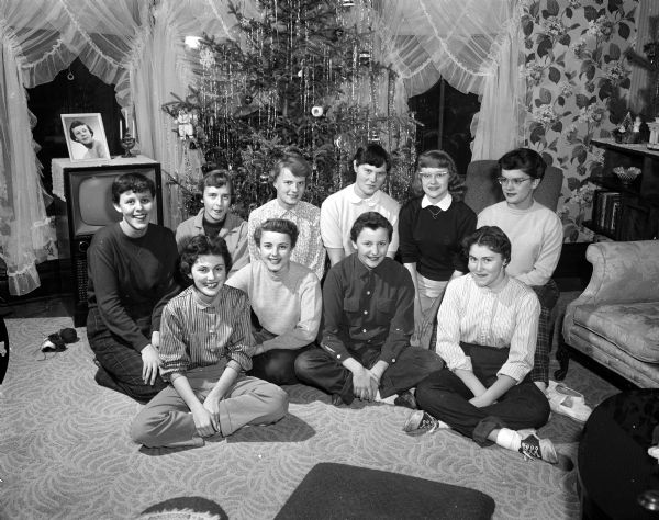 Ten teenage girls gather in front of a Christmas tree at the home of Severa Brevik for a skating and supper party.