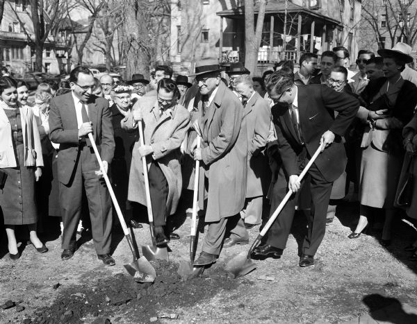 Four men with shovels turn over the first shovels full of earth at 611 Langdon Street, the site of the new Jewish student center. "Left to right are Rabbi Mas Ticktin, directer of Hillel Foundation; Gordon Smykin, president of the building corporation; Irving Rhodes, Milwaukee, a leader in the fund raising campaign, and I.J. Behr, Rockford, Ill., vice-president of the building corporation and brother of the late Louis Behr, for whom the center will be named." Behind them is a crowd.