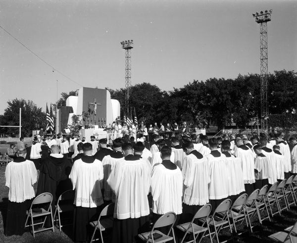 Many priests and altar boys in robes attend a pontifical 'field Mass' at Breese Stevens Field. The Wisconsin Congress of the Confraternity of Christian Doctrine was an organization of lay Catholics that helped priests teach the Catholic religion.