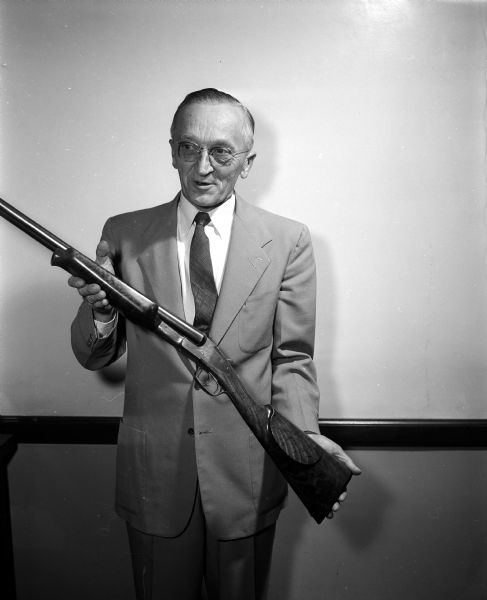 Walter Simon holds his shot gun to show its wooden parts that he crafted himself.  According to his obituary, published on October 18, 1964, he was the Director of Apprenticeship Division of the State Industrial Commission from 1920 to 1960, and a national pioneer in apprenticeship training.