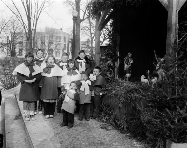 A group of nine children carol at the Nativity crib erected near the Wisconsin State Capitol's State Street entrance by the Madison Deanery Council of Catholic Women, with help from the Knights of Columbus.