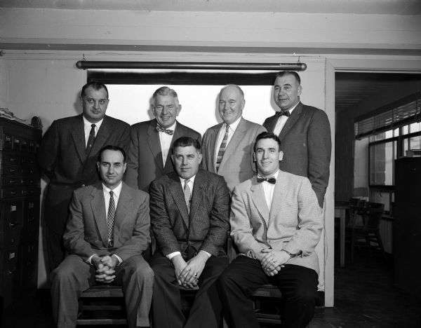 Group portrait of the University of Wisconsin football coaching staff under new head coach, Milt Bruhn. Front row, left to right: La Verne Van Dyke, Milt Bruhn, and Robert Odell. Back row: Paul Shaw, Fred Marsh, Thomas (Red) Hearden, and George Lamphear.