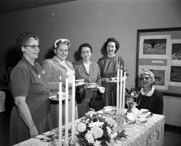 Four ladies stand and one lady sits at a decorated tea table at Washington School.