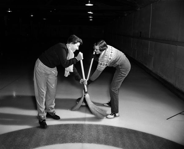 Two members of the West High School Girls' Curling Club demonstrate a sweeping technique. At left is Pat Thomson and right, Mary Stumpf.