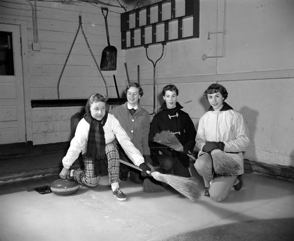 Terry Thomas, left, a member of the West High School Girls' Curling Club, preparing to send a stone down a sheet at the Madison Curling Club. Waiting with their brooms, left to right, are teammates Peggy Welch, Sue Trewartha, and Sue Torrance.