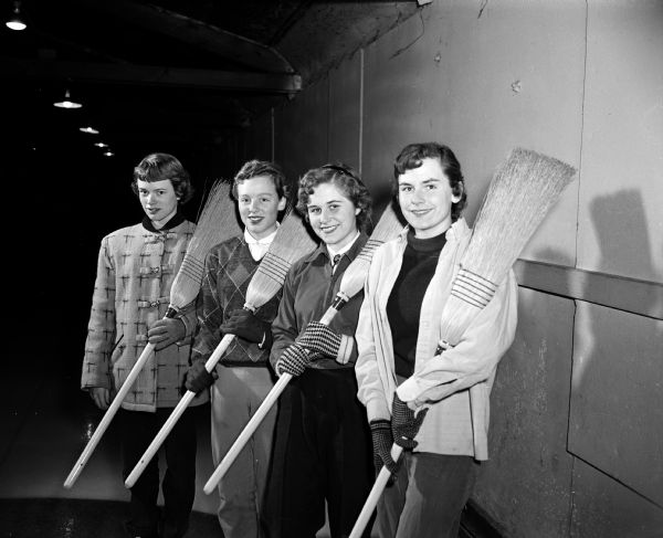 Four members of the West High School Girls' Curling Club holding their brooms. They are, from left: Mary La Duke, Sally Crownhart, Sally Trieloff, and Susie Trieloff.