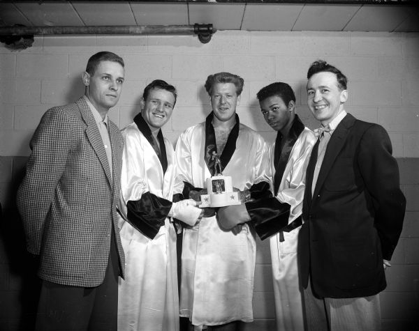 Portrait of three Golden Gloves boxers who will participate in a tournament at Blessed Martin House at 1862 Beld Street in Madison. They are holding a trophy from last year. Pictured are, left to right: coach Bob Brigham, Cod Olson, Ken Kundert, Travis McKoy, and coach Jackie Gibson.