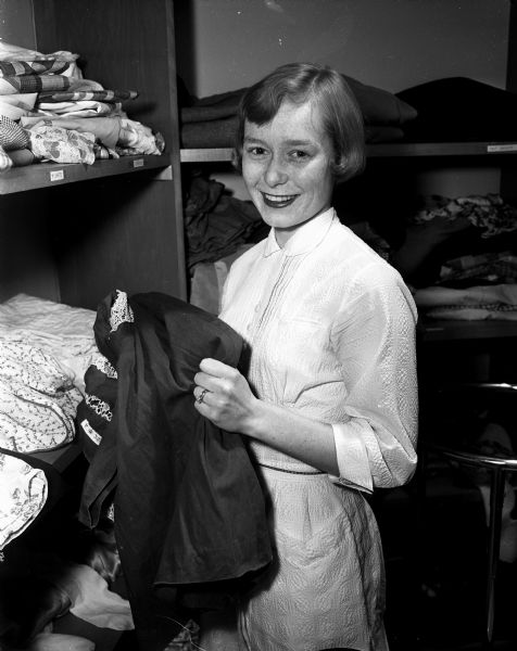 Dagmar Kammerer works as a nurse's aide at the Wisconsin Diagnostic Center. Her husband, Dagmar Kammerer, is a senior political science major at the University of Wisconsin. She is shown in a closet selecting clothing for her patients to wear.