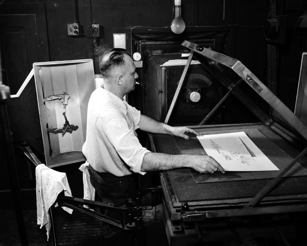 Gilbert Stahl, camera man for Brock Engraving Company, adjusts art in the copy holder. Shown is the camera which will shoot the art; negatives are developed and positioned so zinc plates can be made which go to the engraver.