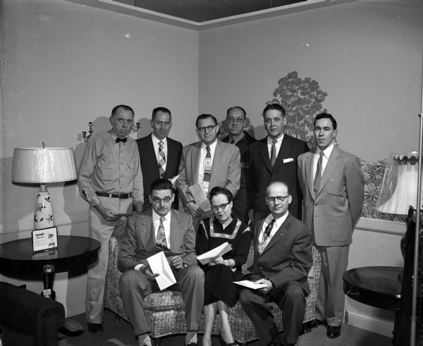 Group portrait of the nine members longest in standing in the Madison Sears, Roebuck and Company "savings and profit-sharing pension fund." They are, left to right, first row: Lester Daley, Ruth Staebler, and Clifford Helbring. In the back row are: Ole Selje, Howard Lippencott, Stanley Hagen, Walter Krause, George Schoen, and Pat Terry. Five of them are holding envelopes containing statements showing their personal total assets in the fund.