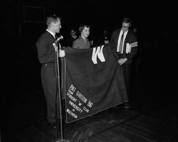 Pat Gibson, World Senior Women's Speed Skating Champion, receives a W blanket award from the Student W Club. Jack Nowka is at left and Jack Mansfield is beside him.