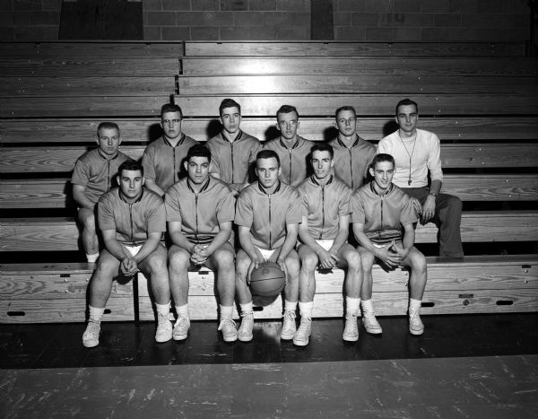 Group portrait of the Oregon Basketball Team in uniform. They pose with their coach, seated in bleachers.