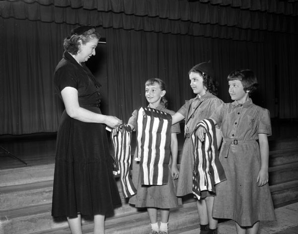 Three flags are presented to the Brownie troops at Schenk School by members of the American Legion Auxiliary. Madelynn Suthers, president of the auxiliary to William B. Cairns Victory Post No. 57, presents flags to Sandy Lee St Arnaulds, Linda Cutler, and Marie Rasmussen.