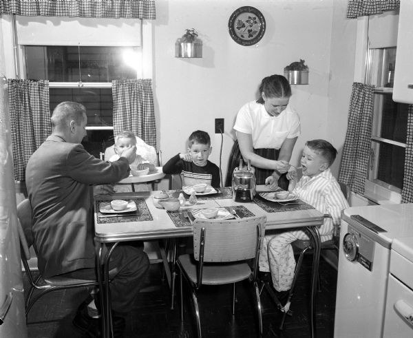 The family of David Lindl, the 1956 "Easter Seal Boy", eating breakfast. They include, from left: father Frank C. Lindl; Dennis, age 17 months; mother Margaret; and David, age 6. David, who has muscular dystrophy, was chosen to represent handicapped men, women, and children in Dane County whom the Easter Seal Society hopes to aid through the sale of its seals.