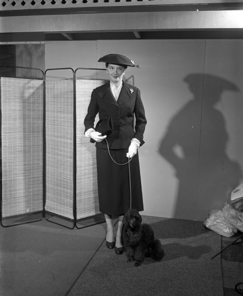 Louise Romaker, representing the Wisconsin Vererinary Medical Auxiliary, models fashion for the 'smart clubwomen.' She is accompied by her poodle, Cherie. The proceeds of the style shows were to maintain and further the services to those with cerebral palsy living in Madison and Wisconsin.