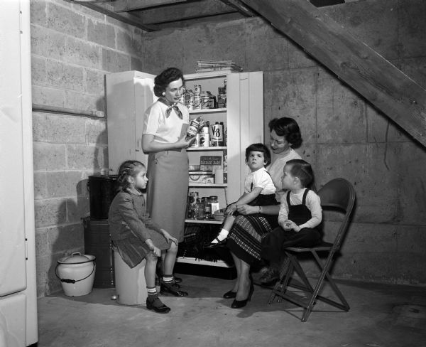 Mary Hogan, Katherine Becker, and children posing near the Hogan's home civil defense shelter. Hogan and Becker are members of the Dane County Medical Auxiliary which encourages its members to have these shelters in their homes.