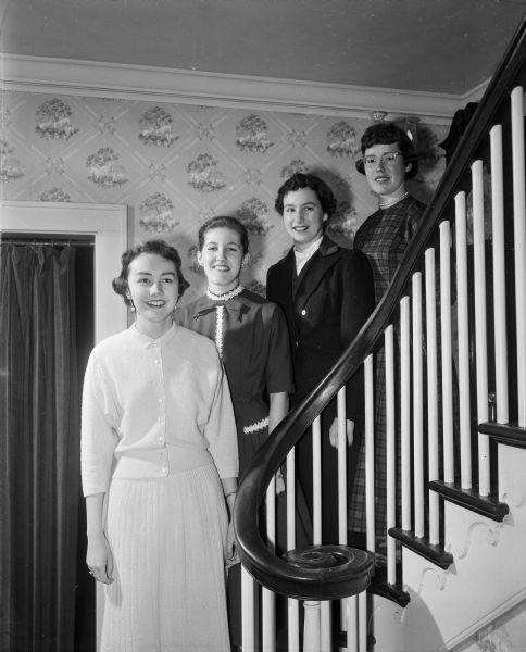 Group portrait of four high school students standing on a staircase, the 1956 winners of the Good Citizenship pins awarded by the John Bell chapter of the Daughters of the American Revolution. Left to right: Sybil Kay Berntson, East High; Sue Parisi, Central High; Peggy Miller, Wisconsin High; and Ann Louise McGibbon, West High.